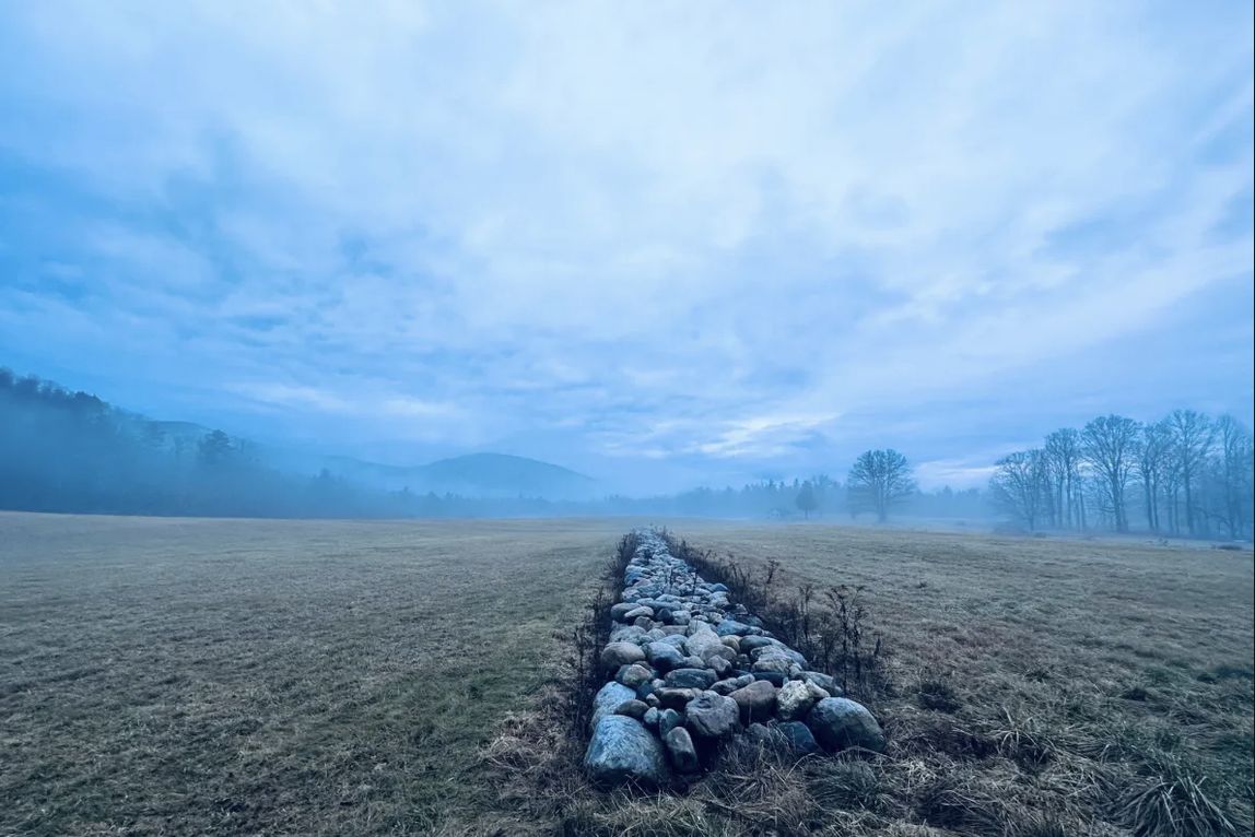 Stone wall across a misty field toward the mountains